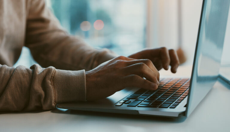 Close-up of a person typing on a laptop keyboard in a softly lit indoor setting.