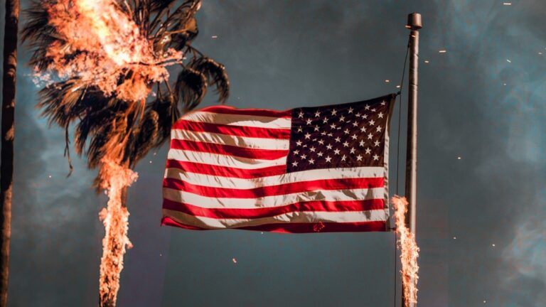 American flag flying on a pole with a burning palm tree and flames in the background.