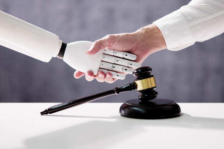 Human hand shaking robotic hand over a judge's gavel on a white table.