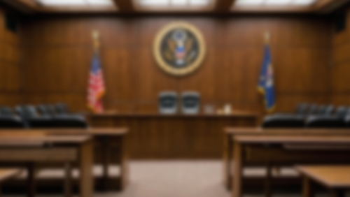 Interior of a courtroom with wooden furniture, American flags, and a judicial seal on the wall.