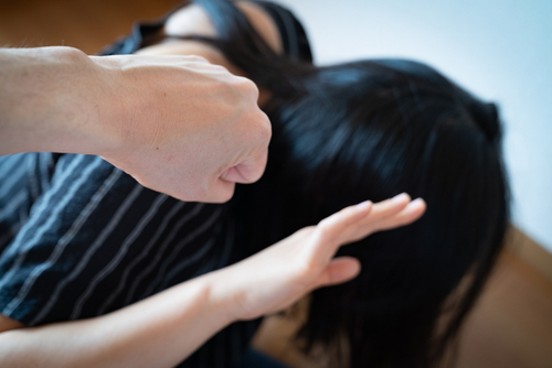 Close-up of a raised fist near a person shielding their head with hands, indoors.