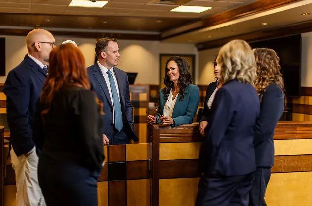 A group of professionally dressed individuals engaged in conversation inside a courtroom setting.