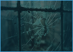 Close-up of a broken glass window with multiple cracks and a central hole.