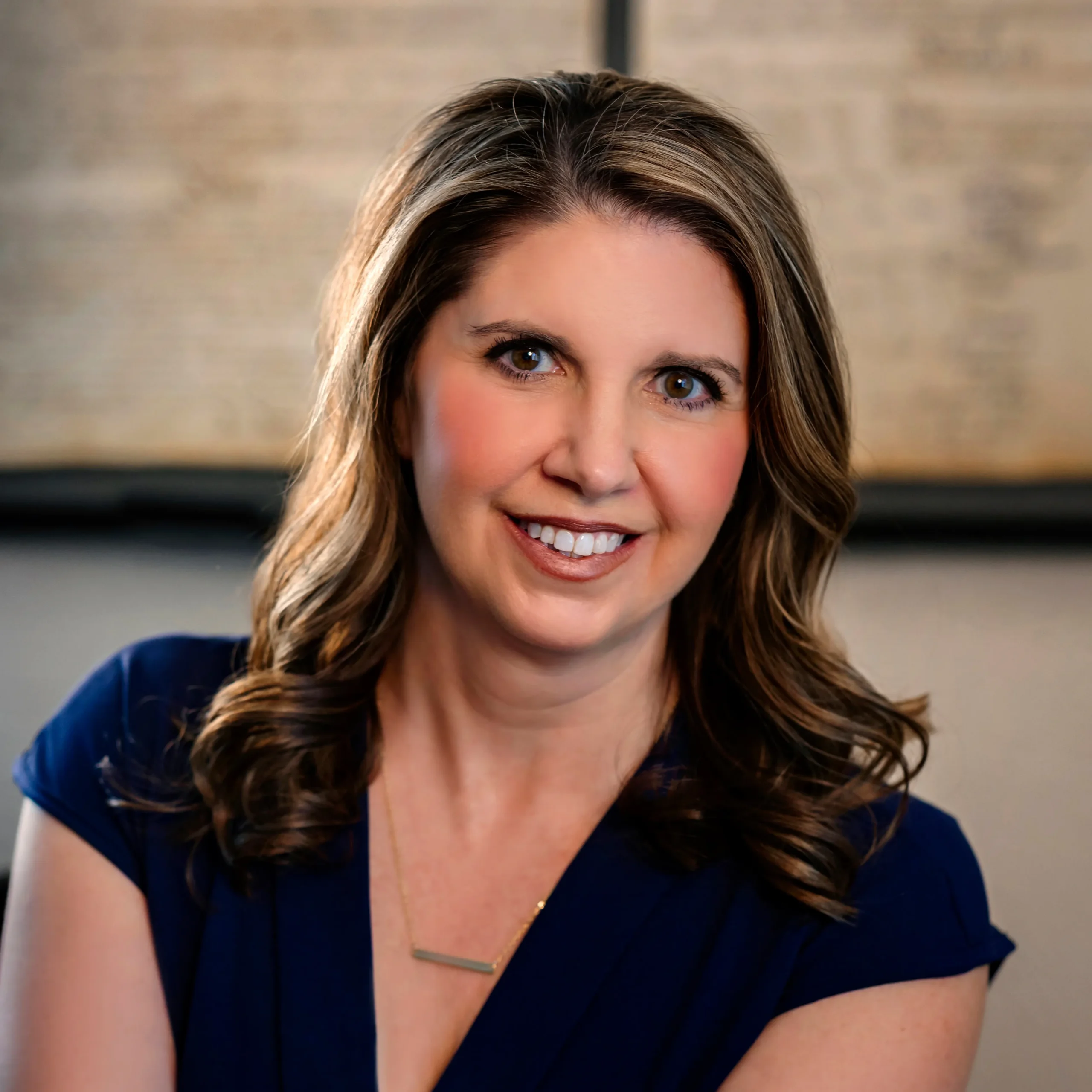 Professional headshot of a smiling woman with wavy brown hair wearing a navy blue top.