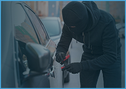 Person dressed in black hoodie and gloves attempting to break into a car with tools.