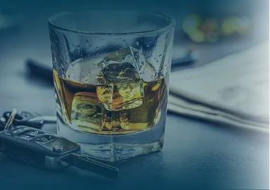 Glass of whiskey with ice cubes placed on a table beside a car key and newspaper.