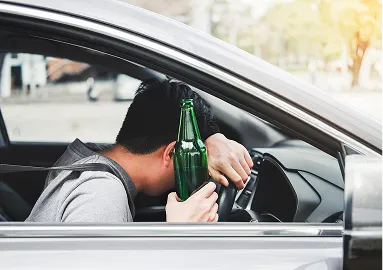 Man sitting in a silver car holding a green glass bottle, appearing distressed.