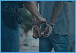 A police officer handcuffing a person wearing a gray shirt and blue jeans.