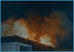 Fire engulfing the roof of a residential building at night with thick smoke.