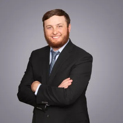 Professional portrait of a smiling man in a black suit with crossed arms.