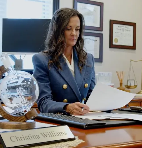 Professional woman in blue blazer reviewing documents at office desk with nameplate "Christina Williams.