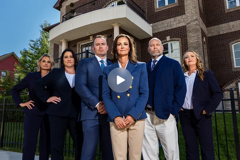 Group of six professionally dressed individuals standing confidently in front of a brick building with columns.