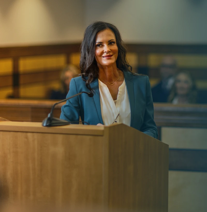 Professional woman in teal blazer speaking at courtroom podium with microphone.