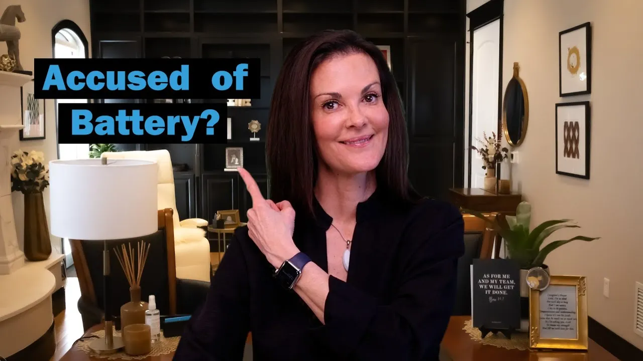 Woman in black shirt pointing to text "Accused of Battery?" in a modern, well-lit living room.