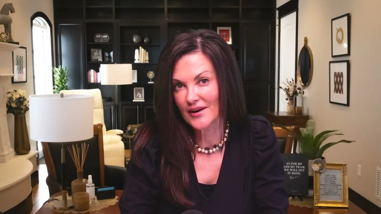 Professional woman with dark hair and pearl necklace sitting in a warmly decorated office.