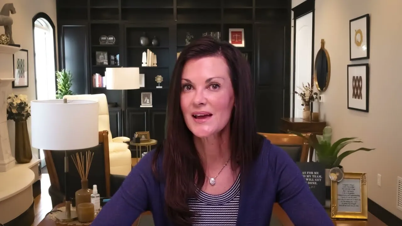 Professional woman with dark hair seated in well-lit modern office with dark shelves and framed art.