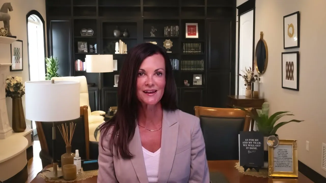 Professional woman with long dark hair in beige blazer seated in modern office with dark bookshelves and decorative items.