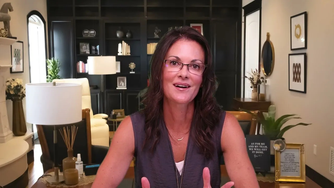Woman with glasses speaking in a home office with dark bookshelves and decorative items.