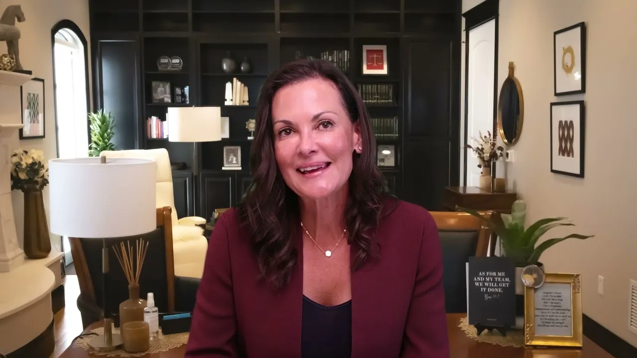 Professional woman with dark hair wearing a burgundy blazer seated in a well-decorated home office.