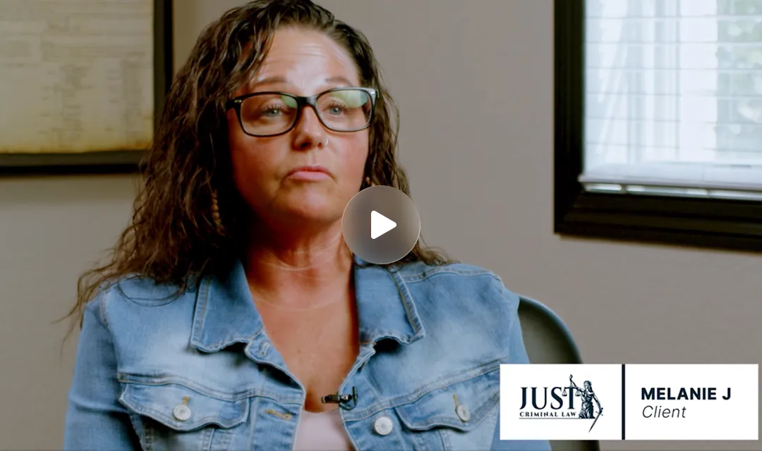 Woman with curly brown hair and glasses wearing a blue denim jacket, seated indoors, with a "Just Criminal Law" logo and text "Melanie J Client" visible.