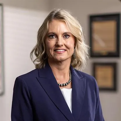 Professional portrait of a smiling blonde woman in a navy blazer and white top.