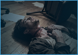 Man lying on wooden floor with blood on neck, appearing injured or unconscious.