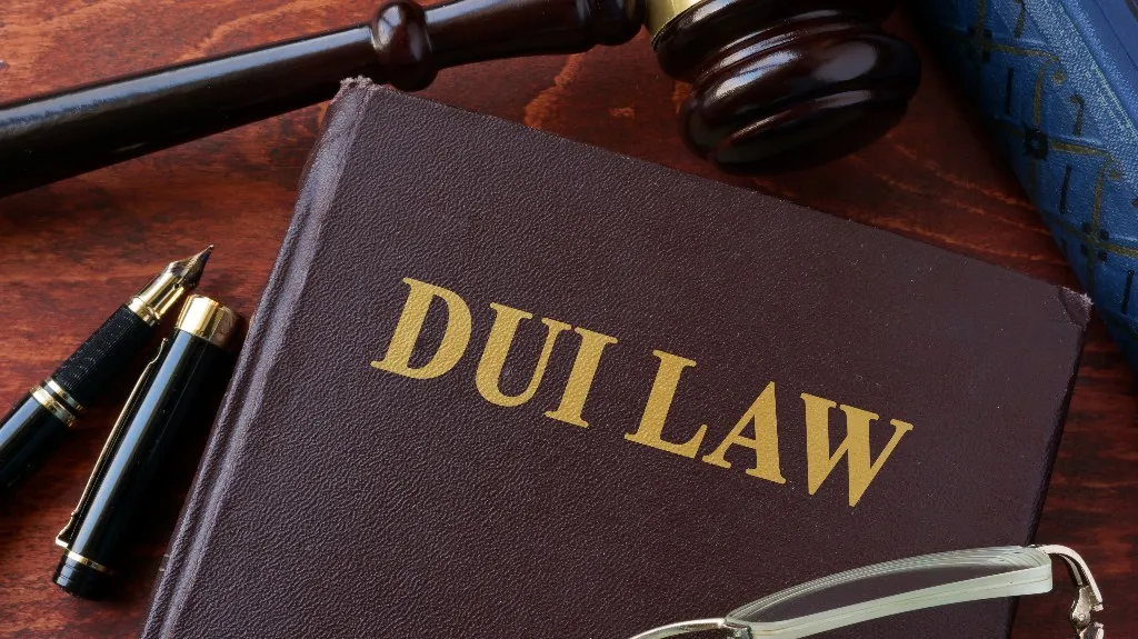 Close-up of a brown book titled "DUI LAW" with a gavel, fountain pen, and eyeglasses on a wooden surface.