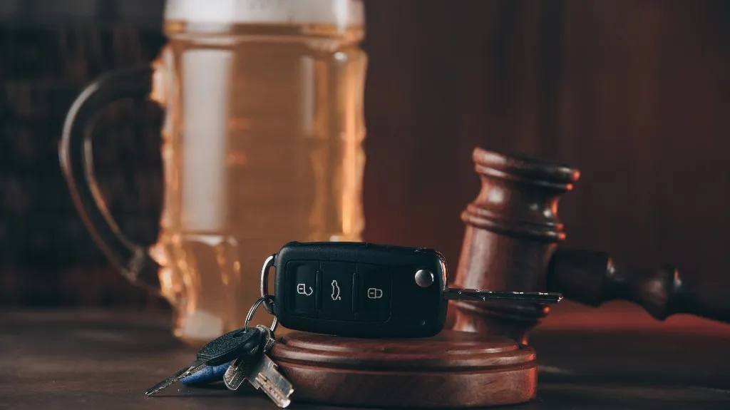 Close-up of a wooden judge's gavel, car key fob, and a glass beer mug on a dark surface.