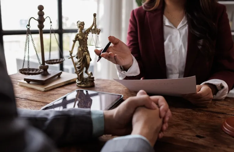 Professional legal consultation with lawyer in burgundy blazer reviewing documents at wooden desk.