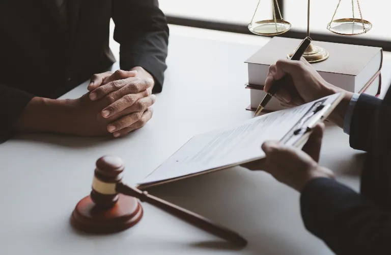 Two individuals in formal attire reviewing and signing legal documents at desk with gavel, law books, and scales of justice.