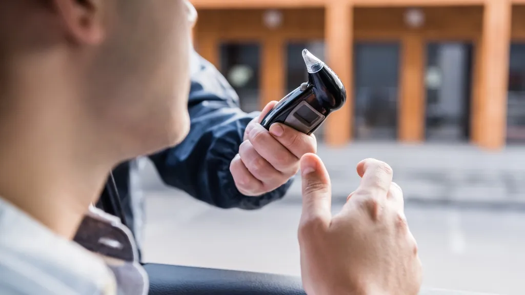 Person undergoing a breathalyzer test with a handheld device outdoors near a building.