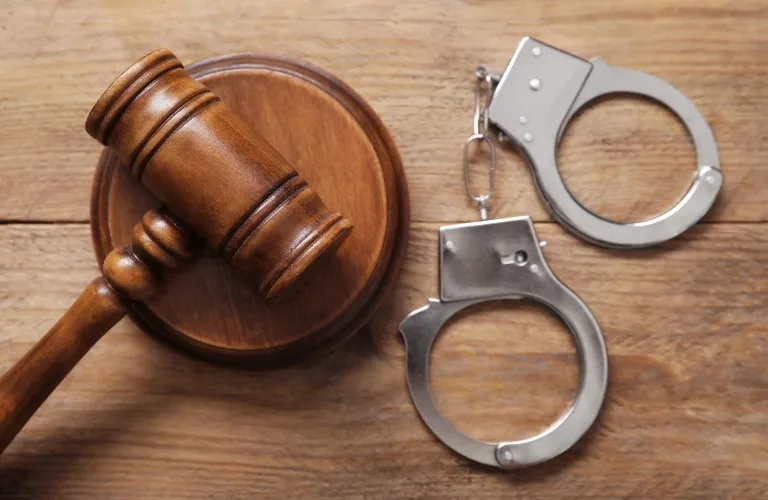Wooden judge's gavel and metal handcuffs resting on a wooden surface.