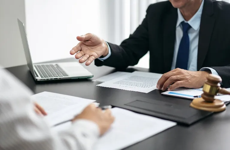 Two professionals in business attire discussing documents at a desk with a laptop and judge's gavel.