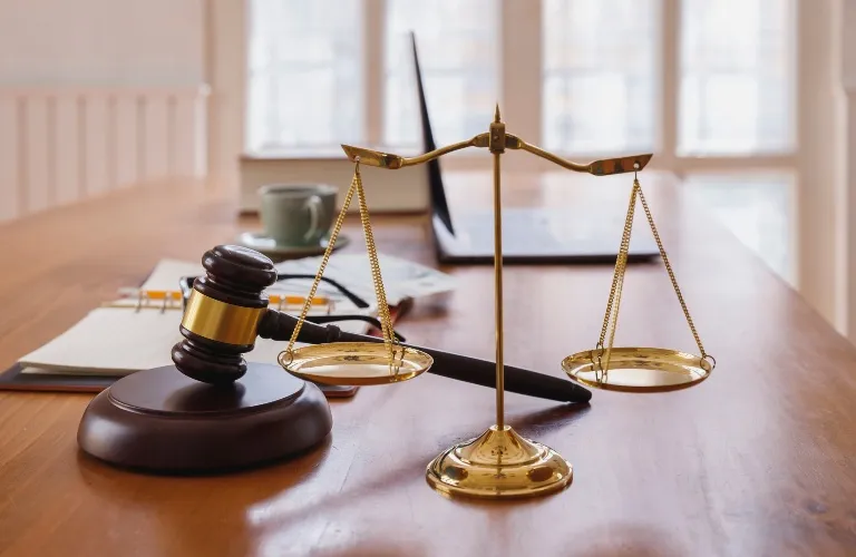 Golden balance scale and wooden judge's gavel on a polished wooden desk with blurred background.