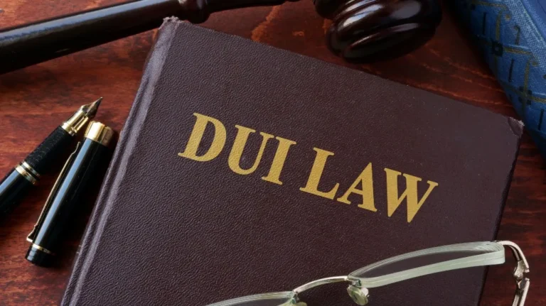 Close-up of a brown legal book titled "DUI LAW" with a fountain pen, eyeglasses, and a wooden gavel.