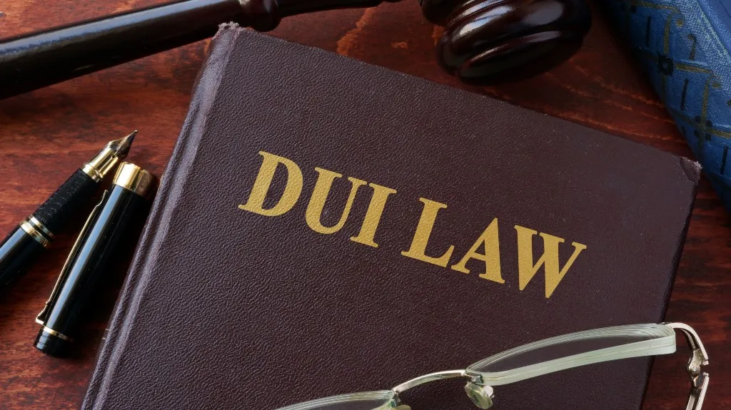Close-up of a brown legal book titled "DUI LAW" with a fountain pen, eyeglasses, and a wooden gavel.