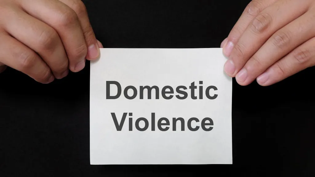 Two hands holding a white paper with the text "Domestic Violence" on a black background.