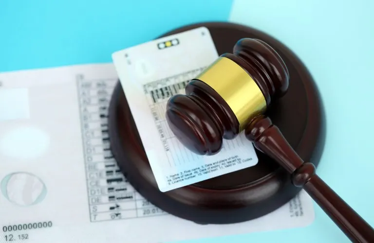 Wooden judge's gavel with gold band resting on identification cards against a light blue background.