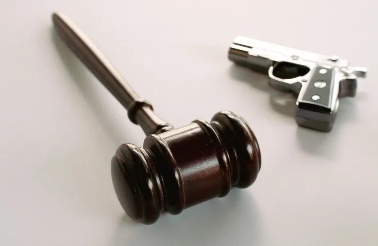 Dark wooden judge's gavel and small silver handgun on a light gray surface.