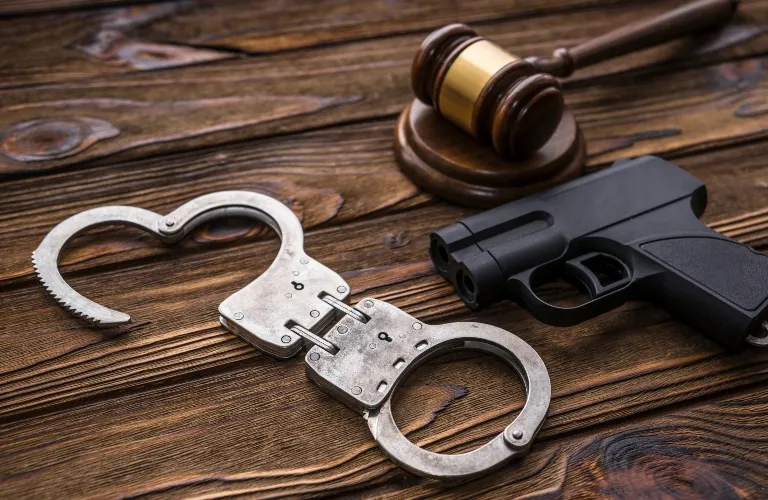 Metal handcuffs, black handgun, and wooden judge's gavel on wooden surface.