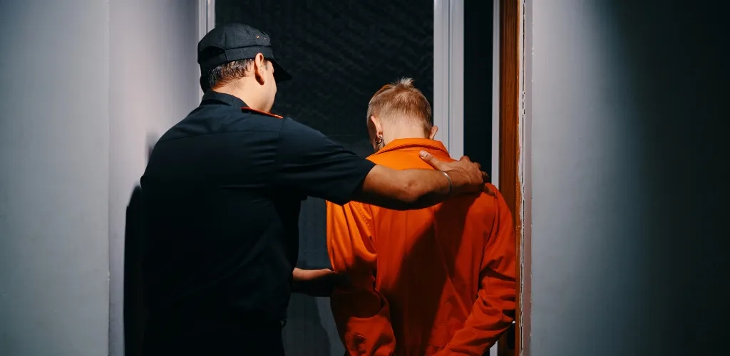 Police officer escorting a person in an orange jumpsuit through a doorway.