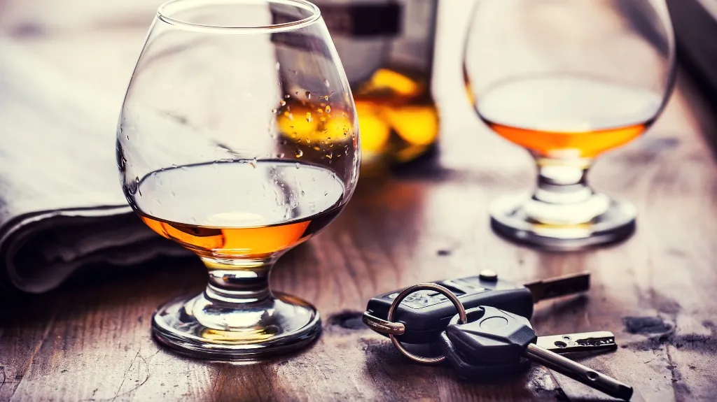 Two snifter glasses with amber liquid and a set of car keys on a wooden table.