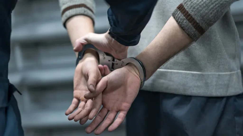 Close-up of a person in handcuffs being held by an officer wearing a dark uniform.